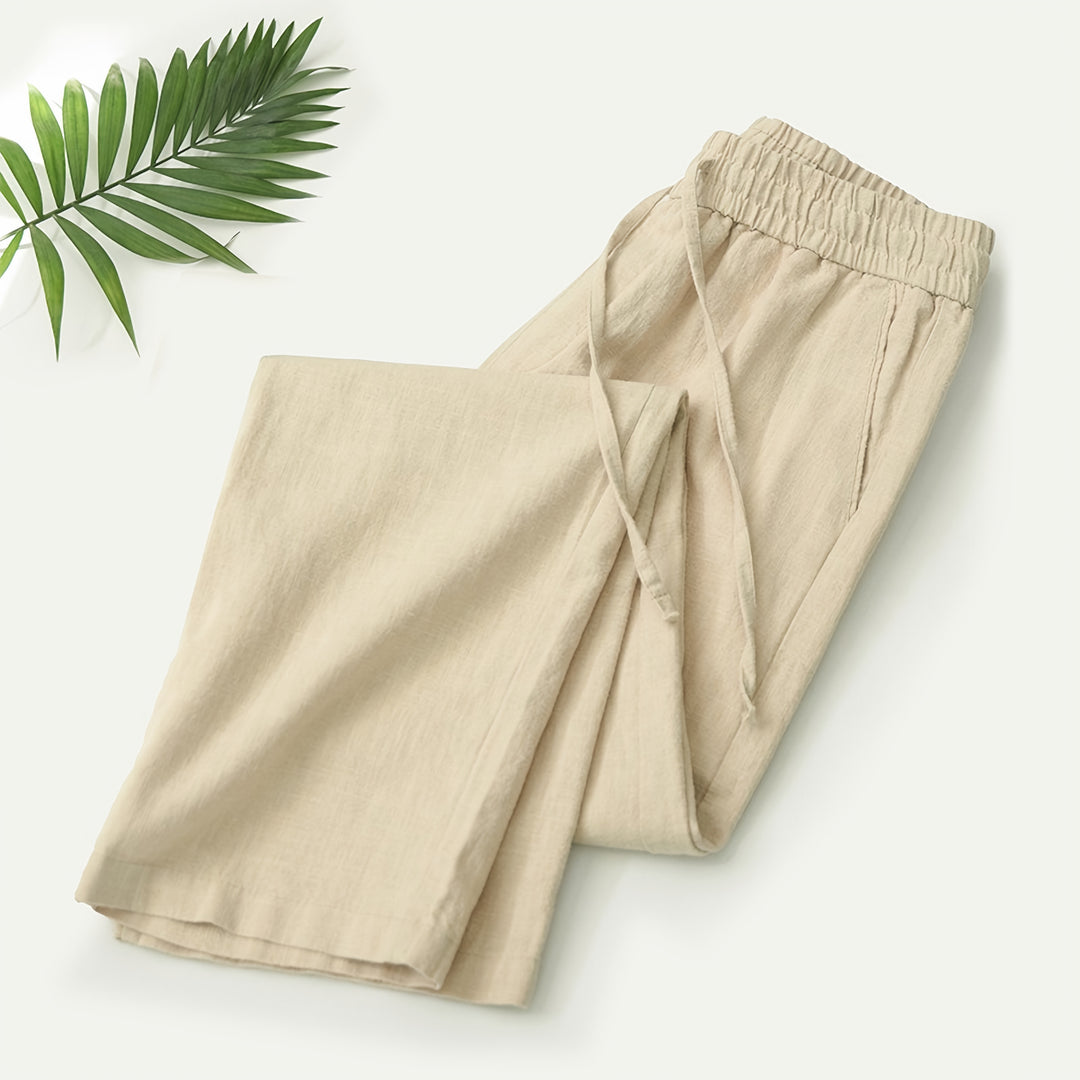 Mann in beiger Sommerhose an einer Strandpromenade mit Leinenhemd und Sandalen