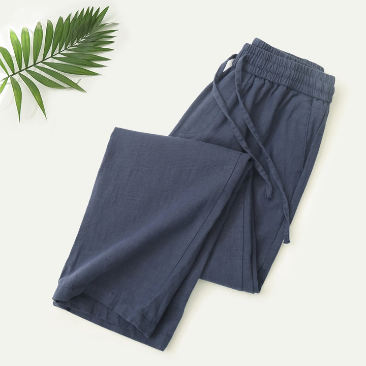 Mann in beiger Sommerhose an einer Strandpromenade mit Leinenhemd und Sandalen