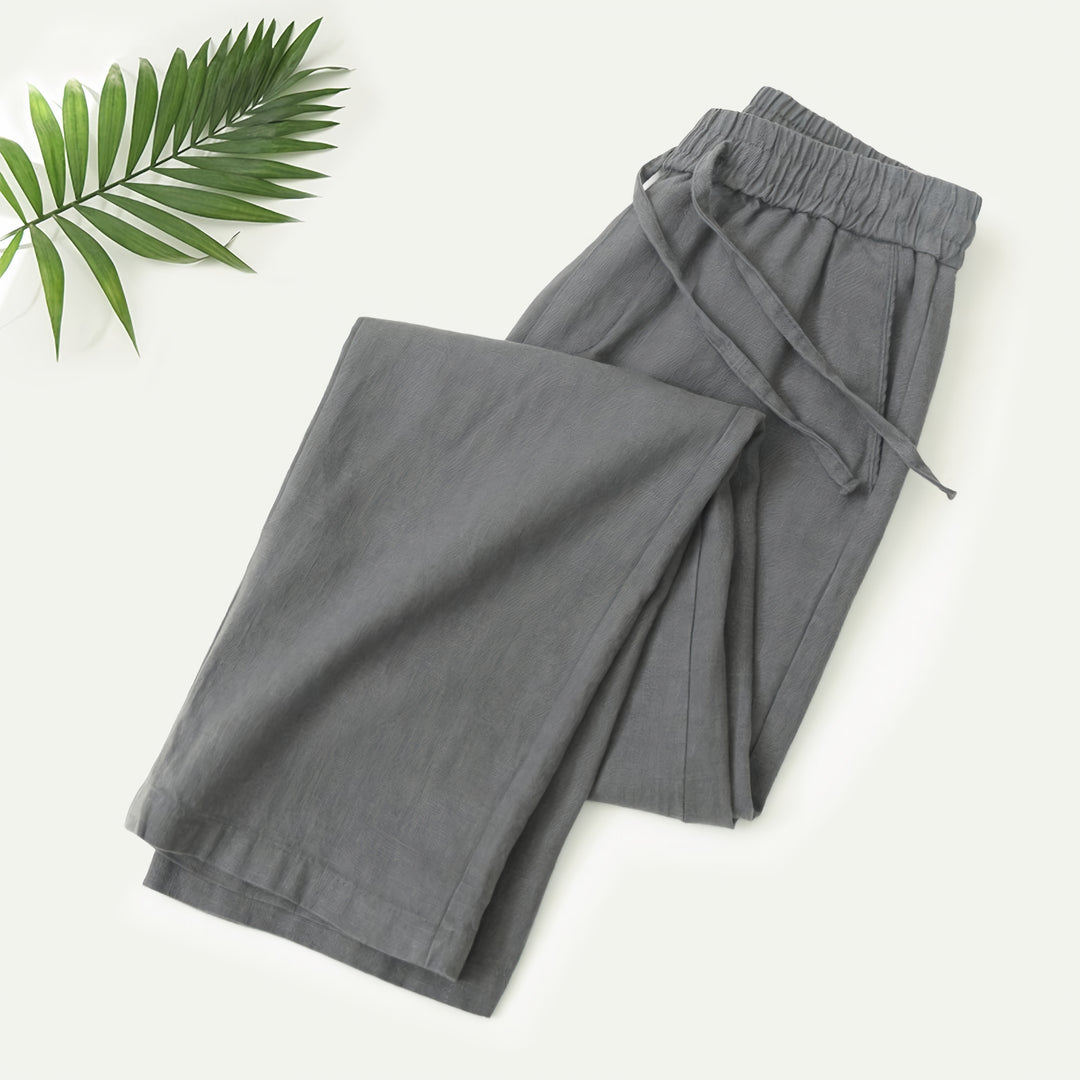 Mann in beiger Sommerhose an einer Strandpromenade mit Leinenhemd und Sandalen