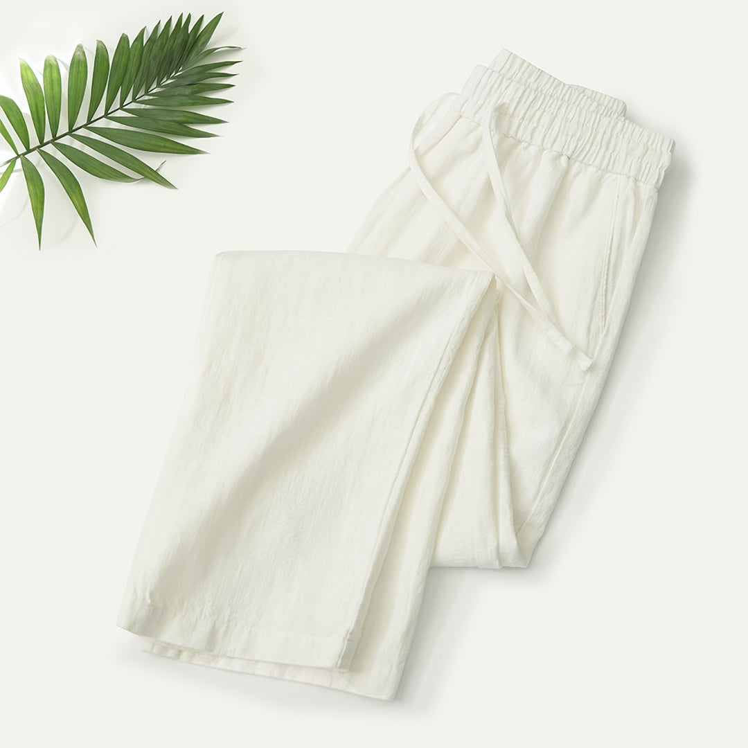 Mann in beiger Sommerhose an einer Strandpromenade mit Leinenhemd und Sandalen