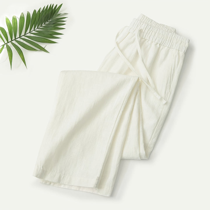 Mann in beiger Sommerhose an einer Strandpromenade mit Leinenhemd und Sandalen