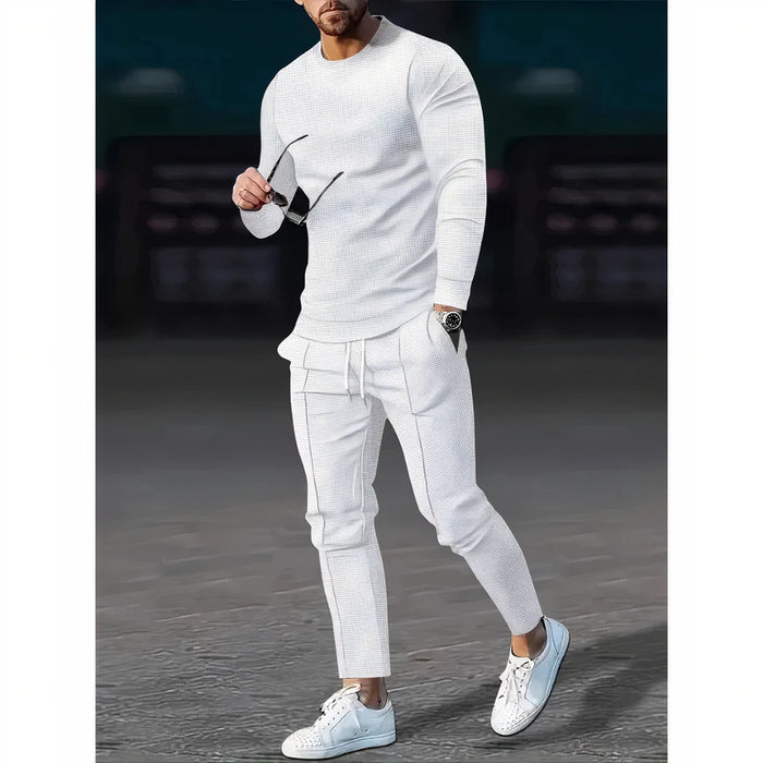 Mann, der ein zweiteiliges Freizeit-Set mit einem Pullover mit Rundhalsausschnitt und einer passenden Hose in einer neutralen Farbe trägt, stehend in einer minimalistischen städtischen Umgebung.