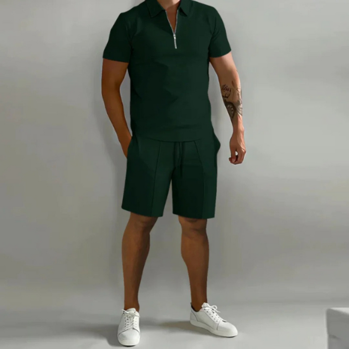 Mann trägt ein passendes Sommer-Kombi-Set mit kurzen Hosen mit Kordelzug und einem Oberteil mit halbem Reißverschluss aus leichtem, atmungsaktivem Stoff.