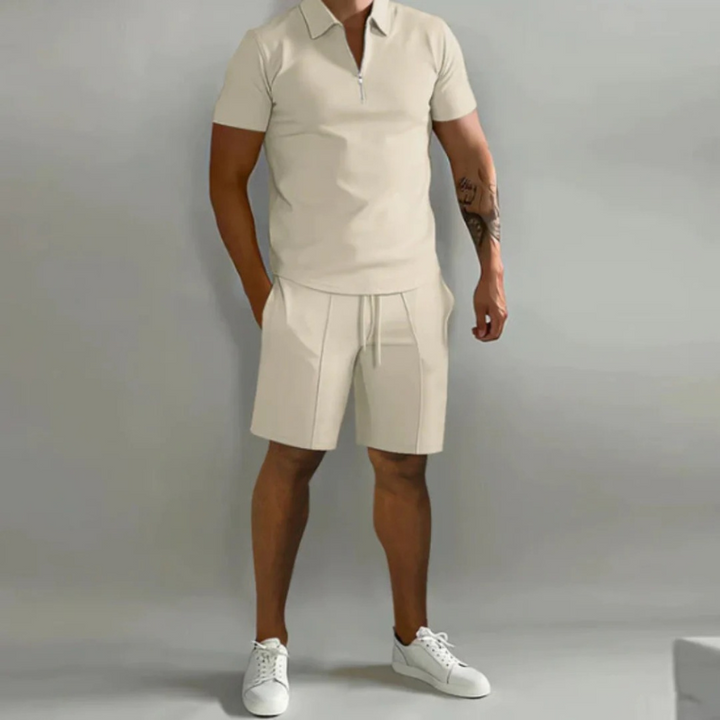 Mann trägt ein passendes Sommer-Kombi-Set mit kurzen Hosen mit Kordelzug und einem Oberteil mit halbem Reißverschluss aus leichtem, atmungsaktivem Stoff.