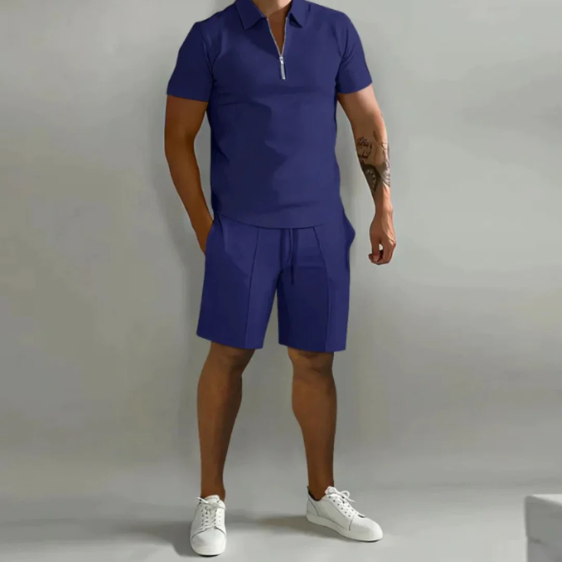 Mann trägt ein passendes Sommer-Kombi-Set mit kurzen Hosen mit Kordelzug und einem Oberteil mit halbem Reißverschluss aus leichtem, atmungsaktivem Stoff.