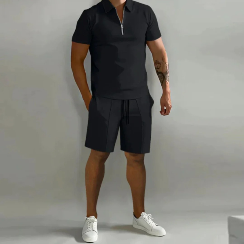 Mann trägt ein passendes Sommer-Kombi-Set mit kurzen Hosen mit Kordelzug und einem Oberteil mit halbem Reißverschluss aus leichtem, atmungsaktivem Stoff.
