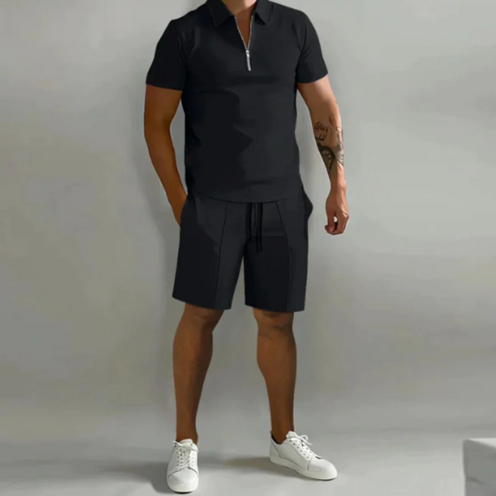 Mann trägt ein passendes Sommer-Kombi-Set mit kurzen Hosen mit Kordelzug und einem Oberteil mit halbem Reißverschluss aus leichtem, atmungsaktivem Stoff.