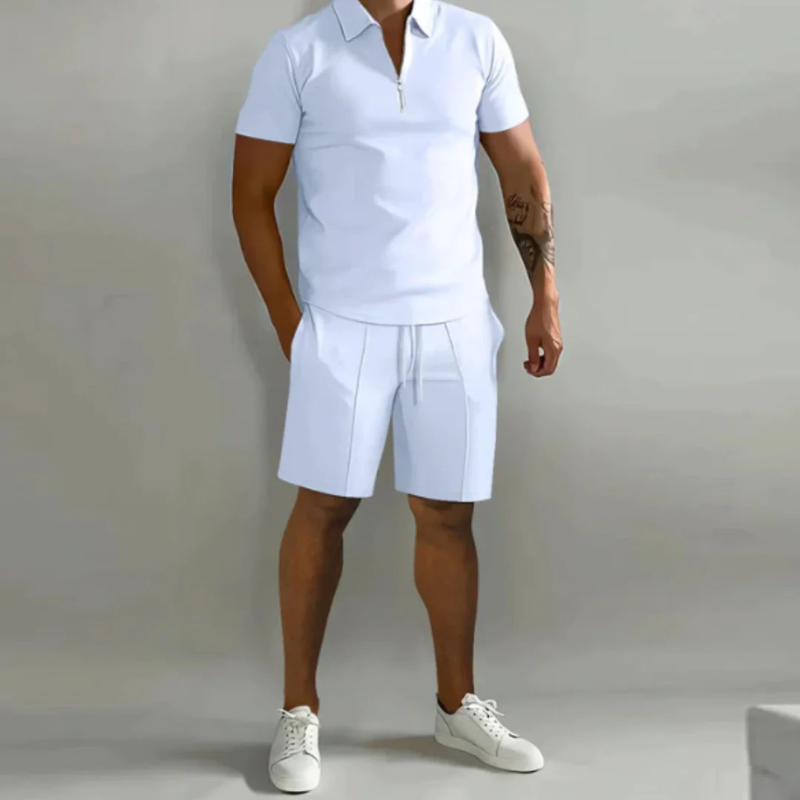 Mann trägt ein passendes Sommer-Kombi-Set mit kurzen Hosen mit Kordelzug und einem Oberteil mit halbem Reißverschluss aus leichtem, atmungsaktivem Stoff.