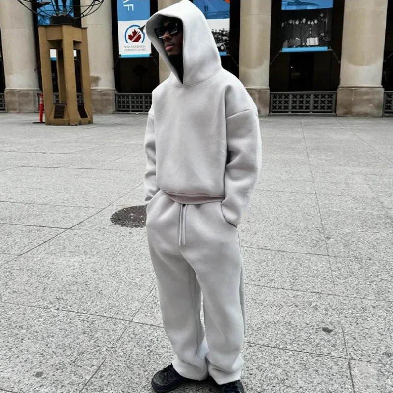 Mann, der ein entspanntes zweiteiliges Lounge-Set mit einem Kapuzenpulli und einer Jogginghose in einer gedeckten Farbe trägt und in einer lässigen Umgebung im Freien steht.