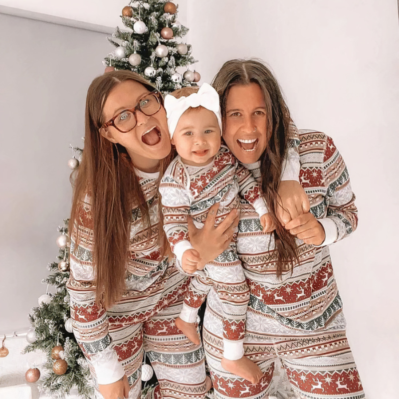 Lächelnde Familie in passenden Weihnachtspyjamas, versammelt in einem gemütlichen Wohnzimmer.